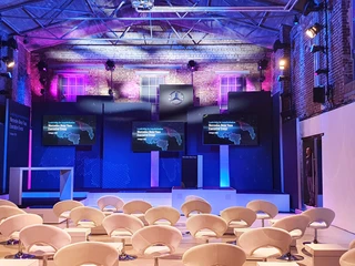 Halle_Produkteinführung Innenraum eines modernen Veranstaltungsraums mit lila Beleuchtung und weißen Sesseln.Interior of a modern event room with purple lighting and white armchairs.