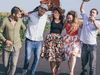 reinakustisch-akustikband-event-party-26.jpg Menschen laufen fröhlich auf einer Straße, ein Mann trägt eine Gitarre, andere lachen und feiern.People walk happily along a street, a man carries a guitar, others laugh and celebrate.