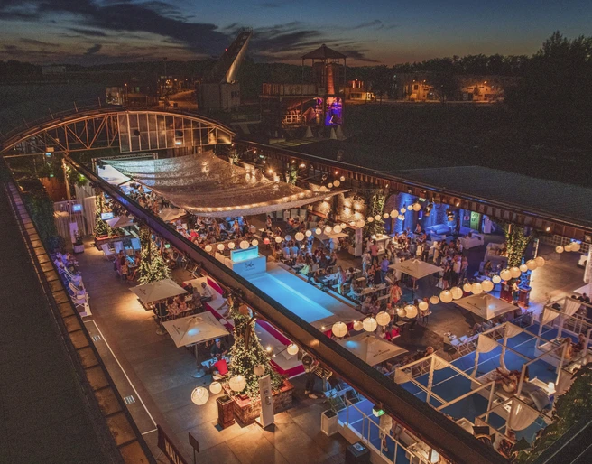 Biergarten der HALLE Tor 2 - Open Air Offene Terrasse eines Restaurants bei Nacht mit stimmungsvoller Beleuchtung und vielen Gästen.Open terrace of a restaurant at night with atmospheric lighting and many guests.