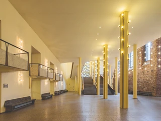 Gürzenich Köln, Erdgeschoss-Foyer  Leerer, lichtdurchfluteter Saal mit Marmorelementen, Treppenaufgang und modernen Leuchten.Empty, light-flooded hall with marble elements, staircase and modern lighting.