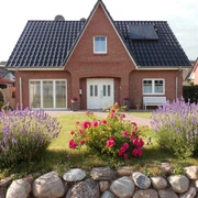 Titelbild Ein Backsteinhaus mit Solarpanelen, umgeben von Lavendel und Rosen in einem gepflegten Garten.