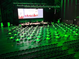 Consilium_live_23_002.jpg Ein großer Veranstaltungsraum mit vielen Stühlen und Tischen, in grünem Licht beleuchtet.</p>A large function room with lots of chairs and tables, illuminated in green light.</p> <p