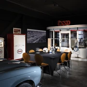 04_CC_PrivateDinner.jpg Retro-Essenzapfsäule und Esso-Diner mit Oldtimer-Motorrad in einem nostalgischen Ausstellungsraum.Retro petrol pump and Esso diner with vintage motorcycle in a nostalgic showroom.