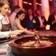 Casino Vinophil. Rebsorten Roulette. Dieter Jacobi.jpg Roulettetisch in edlem Casino, im Hintergrund Gäste und Croupier unter warmem Licht.Roulette table in a classy casino, in the background guests and croupier under warm light.