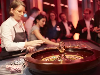 Casino Vinophil. Rebsorten Roulette. Dieter Jacobi.jpg Roulettetisch in edlem Casino, im Hintergrund Gäste und Croupier unter warmem Licht.Roulette table in a classy casino, in the background guests and croupier under warm light.