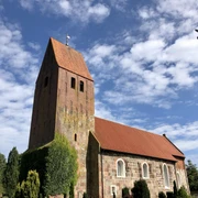 IMG_2933.jpg Backsteinkirche mit hohem Turm, umgeben von blauem Himmel und grünen Sträuchern.