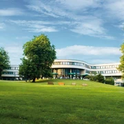Best Western Plus Parkhotel Velbert Modernes Hotelgebäude umgeben von einer weitläufigen, grünen Parklandschaft mit Sitzbänken.