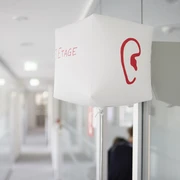 SINNfonie. Ein Parcours durch die Welt de Sinne Ein Flur mit moderner Beleuchtung und einem roten Ohrsymbol auf einer weißen Leuchte.A hallway with modern lighting and a red ear symbol on a white luminaire.