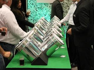 SINNfonie. Eine Parcours durch die Welt der Sinne. Taststation Stahlkessel in zwei Reihen mit Papier an einem Messestand, umgeben von Menschen in Anzügen.SINNfonie. A tour through the world of the senses. Touch station