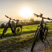 Zwei Fahrräder stehen auf einem Feldweg bei Sonnenuntergang, umgeben von grünen Wiesen.