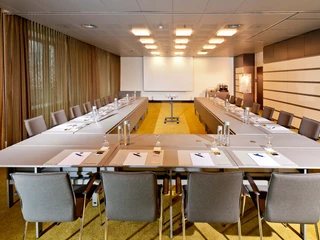 Martin + Augustin  Ein moderner Konferenzraum mit U-förmig aufgestellten Tischen und lederbezogenen Stühlen.A modern conference room with U-shaped tables and leather-covered chairs.