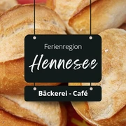 Bäckerei Ferienregion Hennesee Mehrere goldbraune Brötchen sind übereinander gestapelt, beschriftet als "Ferienregion Hennesee".