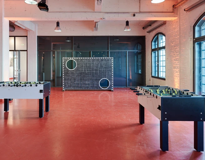 Activity Feld (18).jpg Zwei Tischkicker stehen in einem Raum mit roten Böden, Fenster und ein großformatiges Zielspielgerät.</p>Two table football tables stand in a room with red floors, windows and a large-format target game machine.