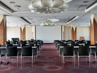 Belvedere  Moderner Konferenzraum mit Reihen von schwarzen Stühlen, Tischen und großer Leinwand im Hintergrund.</p>Modern conference room with rows of black chairs, tables and a large screen in the background.</p> <p