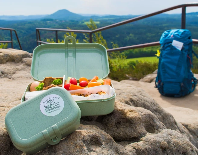 BrotZeit auf dem Zirkelstein Wanderausblick auf Felsen mit Brotbox und Rucksack; malerische Landschaft der Sächsischen Schweiz.