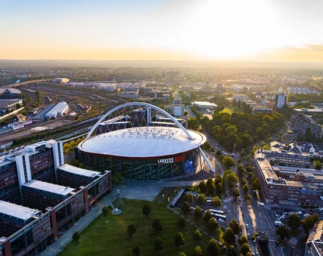 Bild Arena Luftaufnahme des LANXESS arena in Köln bei Sonnenuntergang, umgeben von städtischer Architektur.</p>Aerial view of the LANXESS arena in Cologne at sunset, surrounded by urban architecture.</p> <p