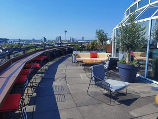 Bar Botanik Außenbereich.jpg Rooftop-Terrasse mit bunten Sitzmöbeln und Blick auf Kölns Stadtpanorama bei klarem Himmel.</p>Rooftop terrace with colorful seating and a view of Cologne's city panorama on a clear day</p>.