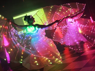 Dancers Lichteffekt-Tänzerinnen mit leuchtenden Flügeln in schimmernden Kostümen auf einer Bühne.Light-effect dancers with glowing wings in shimmering costumes on a stage.