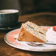 Kuchen und Kaffee Ein Stück Kuchen mit Sahne und Erdbeere auf einem Teller, daneben eine Tasse Kaffee auf einem Holztisch.