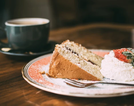 Kuchen und Kaffee Ein Stück Kuchen mit Sahne und Erdbeere auf einem Teller, daneben eine Tasse Kaffee auf einem Holztisch.