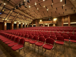 Kulturzentrum_grosser_Saal_083.jpg Ein leerer Konzertsaal mit roten Stühlen und beleuchtetem Holzboden unter einer gewölbten Decke.</p>An empty concert hall with red chairs and an illuminated wooden floor under a vaulted ceiling.</p> <p