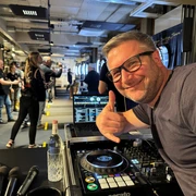DJ Mr. Easy Ein DJ mit Brille vor einem Mischpult, das eine Veranstaltung mit Leuten im Hintergrund zeigt.</p>A DJ with glasses in front of a mixing desk showing an event with people in the background.</p> <p