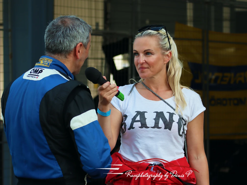 Linda Terting Rennfahrer spricht mit einer Reporterin; er trägt einen blauen Rennanzug, sie hält ein Mikrofon.Racing driver talking to a reporter; he is wearing a blue racing suit, she is holding a microphone.
