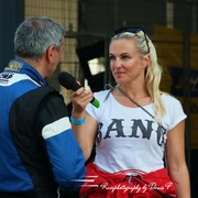 Linda Terting Rennfahrer spricht mit einer Reporterin; er trägt einen blauen Rennanzug, sie hält ein Mikrofon.Racing driver talking to a reporter; he is wearing a blue racing suit, she is holding a microphone.