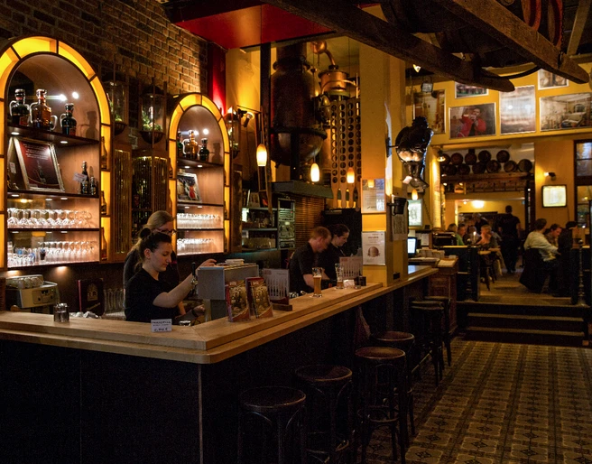 Hellers_Brauhaus_Titel Die Bar im warmen Licht, mit Holzmöbeln und Gästen, strahlt gemütliche Atmosphäre aus.The bar in warm light, with wooden furniture and guests, radiates a cozy atmosphere.