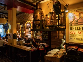 hellers-brauhaus-005.JPG Eine gemütliche Brauhaus-Szene zeigt Menschen an einer Bar, umgeben von Brauereiausrüstung.A cozy brewery scene shows people at a bar surrounded by brewery equipment.