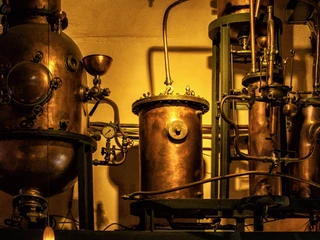 hellers-brauhaus-007.JPG <p>Kupferne Destillationsanlage mit Rohren, Ventilen und Manometern in warmer Beleuchtung.</p><p>Copper distillation unit with pipes, valves and pressure gauges in warm lighting.</p>