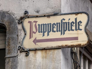 Hänneschen Theater Schild mit "Puppenspiele", an einer Gebäudewand angebracht.Sign with "Puppenspiele", attached to a building wall.