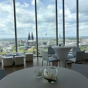 Firmenfeier_KölnSKY Blick aus Panoramafenster auf die Kölner Skyline mit Dom, Fluss und Wolkenhimmel.</p>View from the panoramic window of the Cologne skyline with cathedral, river and cloudy sky.</p> <p
