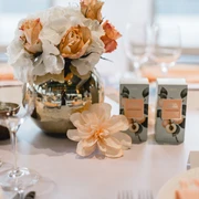 4711 Duftmenü Blumenvase mit Rosen und weißen Blumen auf einem elegant gedeckten Tisch, umgeben von Weingläsern.Flower vase with roses and white flowers on an elegantly laid table, surrounded by wine glasses.