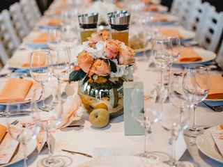 4711 Duftmenü Tisch Tisch mit weißer Tischdecke, dekoriert mit orangefarbenen Servietten und Blumenarrangements.Table with white tablecloth, decorated with orange napkins and flower arrangements.