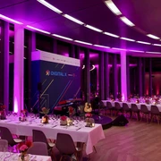KölnSKY_Dinner_Firmenevent Eleganter, in pinkes Licht getauchter Veranstaltungsraum mit gedeckten Tischen und Bühne.</p>Elegant event room bathed in pink light with set tables and stage.</p> <p