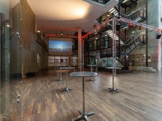 Saal-Foyer Offener Veranstaltungsraum mit Holzboden, Stehtischen und modernen Beleuchtungsanlagen.Open event room with wooden floor, bar tables and modern lighting systems.