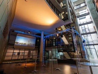 Saal-Foyer Moderner Innenraum mit Bühne, beleuchtet in Blau, und rollstuhlgerechten Zugängen.</p>Modern interior with stage, illuminated in blue, and wheelchair-accessible entrances.</p> <p