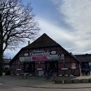 Bild 5.jpg Das Bild zeigt ein traditionelles Fachwerkgebäude mit der Aufschrift "Knuth's Bauernscheune". Fahrräder und eine Sitzbank vor dem Eingang sind erkennbar. Der Himmel ist leicht bewölkt.