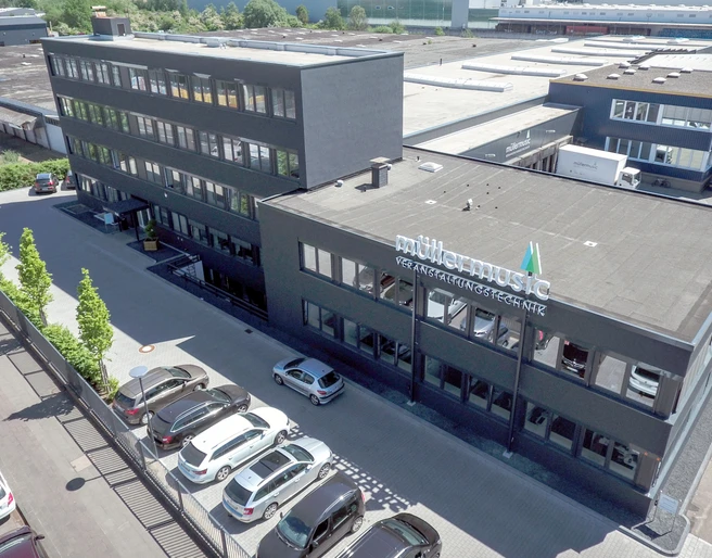 Firmensitz Modernes Bürogebäude mit Schriftzug "Müllermusic" an der Fassade, umgeben von Parkplätzen.</p>Modern office building with "Müllermusic" lettering on the façade, surrounded by parking spaces.</p> <p