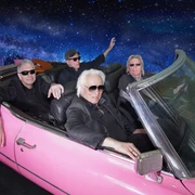 Hannes Schöner Band Vier ältere Männer in Sonnenbrillen fahren in einem pinken Cabrio durch eine Galaxie-Kulisse.Four older men in sunglasses drive through a galaxy backdrop in a pink convertible.