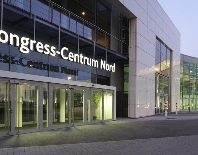 Congress-Centrum Nord Koelnmesse, Eingang Congress-Centrum Nord in Köln, modernes Gebäude bei Dämmerung, mit großen Glasfenstern und hellem Eingang.Congress-Centrum Nord in Cologne, modern building at dusk, with large glass windows and bright entrance.