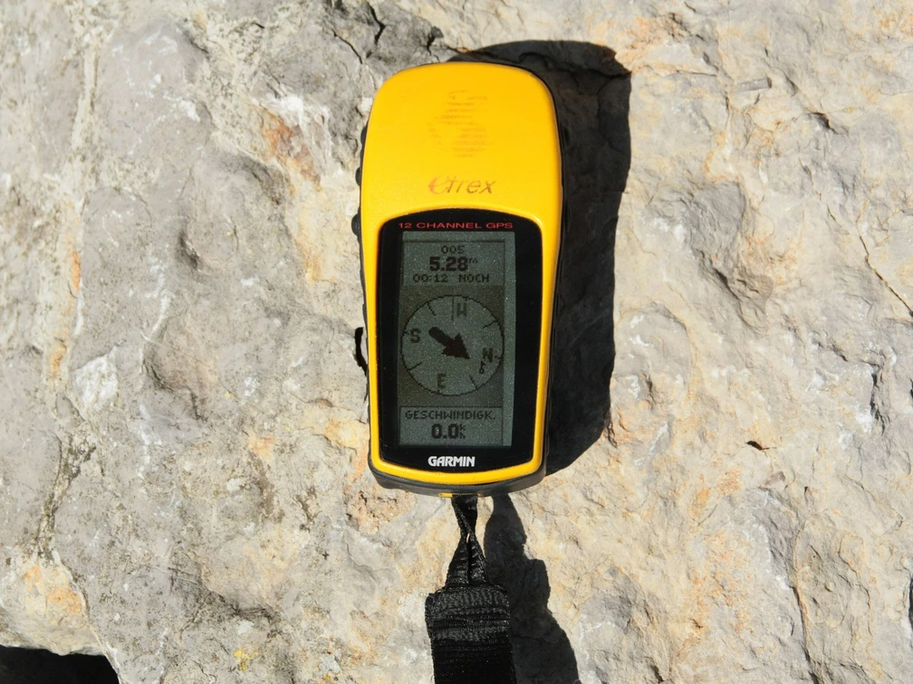 GPS.jpg Leuchtend gelbes, tragbares GPS-Gerät liegt auf einem Felsen in der Sonne. Bildschirm zeigt Kompass.</p>Bright yellow, portable GPS device lying on a rock in the sun. Screen shows compass.</p>