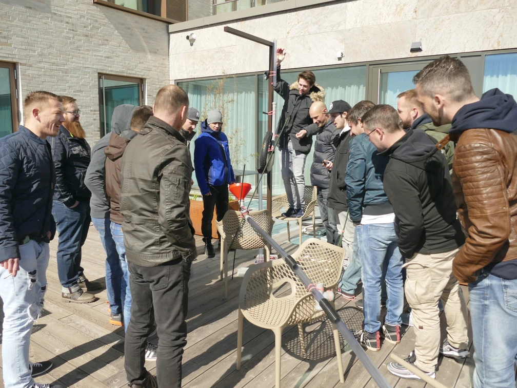 Kugelbahn_Hauptmotiv.jpg Eine Gruppe von Männern baut gemeinsam eine kreative Konstruktion auf einer Holzterrasse.A group of men work together to build a creative construction on a wooden terrace.