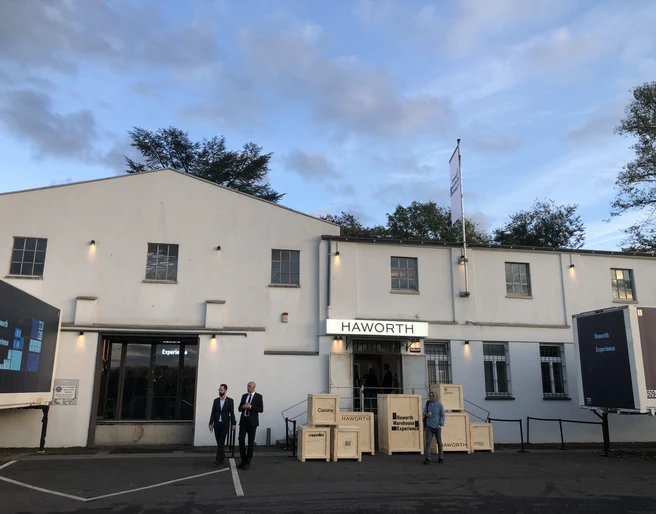 Hafen 12 Graues Gebäude bei Abenddämmerung, Menschen davor, blauer Himmel mit Wolken.</p>Gray building at dusk, people in front of it, blue sky with clouds.</p> <p