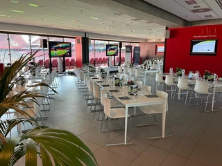 Business-Veranstaltung Elegante Veranstaltungslocation mit gedeckten Tischen, Monitoren und Panoramablick auf ein Stadion.</p>Elegant event location with set tables, monitors and a panoramic view of a stadium.