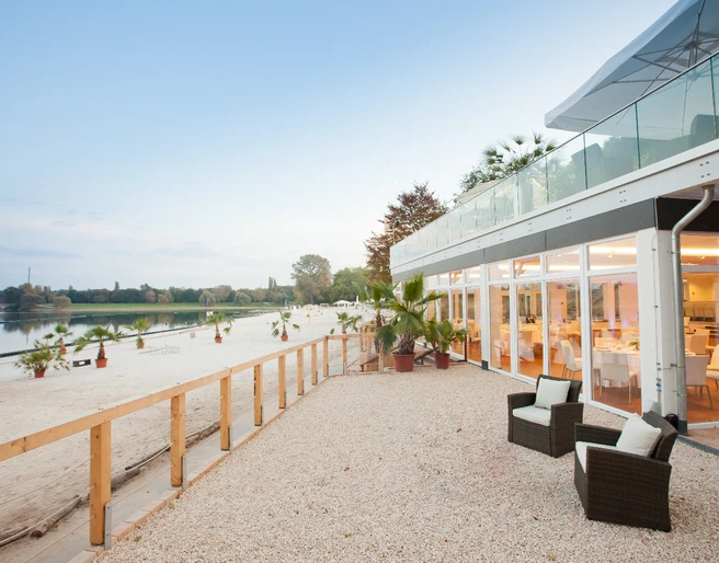 Seepavillon am Blackfood Beach Modernes Strandrestaurant mit Glasfront und Palmen, eingebettet in eine ruhige Seelandschaft.</p>Modern beach restaurant with glass front and palm trees, nestled in a tranquil seascape.</p> <p