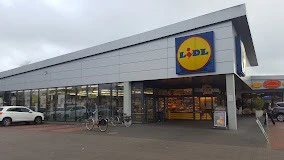 Lidl_Augustfehn_2023.jpg Ein moderner Lidl-Supermarkt mit großem Parkplatz, Fahrradständern, klarer Architektur und dem markanten, blau-gelben Logo.