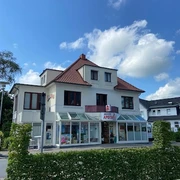 Marien-Apotheke_Augustfehn_2023.jpg Ansicht der Marien-Apotheke Augustfehn, ein zweistöckiges, weißes Gebäude mit roten Dachziegeln.