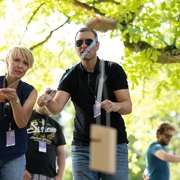 Teambuilding.jpg Teilnehmer werfen Holzstäbe bei einer freundlichen Outdoor-Veranstaltung unter einem Baum.Participants throw wooden sticks under a tree at a friendly outdoor event.